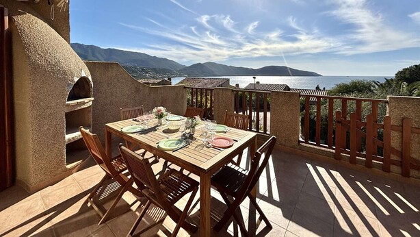 An outdoor dining area with a table set for four, overlooking a scenic view of mountains and a body of water.