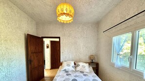 A bedroom with a bed, a wooden door, a window, and a hanging light fixture.