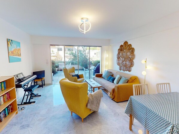 A spacious living room with a piano, sofa, and armchair, a bookshelf, and a view to the outside.