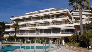 Ett hotell med flera våningar, balkonger, en swimmingpool och palmer.