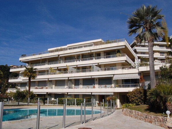 A multi-story hotel with balconies, a swimming pool, and palm trees. - Spacious 3P with air conditioning, terrace in a quiet residence with pool (Menton)