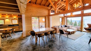 L'intérieur de ce chalet spacieux, avec ses murs en bois, comprend un coin repas, un ensemble de canapés et de grandes fenêtres qui offrent une vue sur l'extérieur.