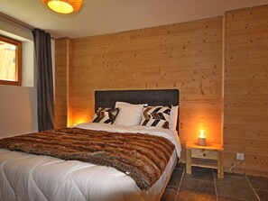 A bedroom with a wooden headboard, a bed with patterned pillows, a bedside table with a lamp, and a window with curtains. - Spacious Renovated Chalet · Terrace · Sleeps 10 · Free Wifi (Les Arcs 1800)