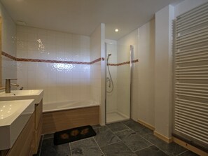 A modern bathroom with two sinks, a bathtub, and a glass-enclosed shower.