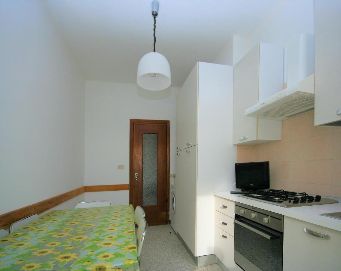 Una habitación pequeña y funcional con cama, kitchenette, puerta y luz en el techo.