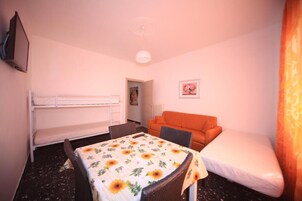 Una habitación pequeña y acogedora con una cama individual, una litera, una mesa con mantel de flores y un sofá.