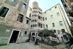 Una calle estrecha con edificios históricos, incluyendo una torre con balcones y una puerta con una valla.