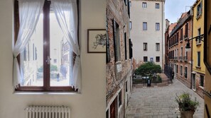 A narrow courtyard with a view from a bedroom, featuring a radiator, a window with sheer curtains, and a framed picture on the wall. - SPIRAL-Canal-View (Venice)