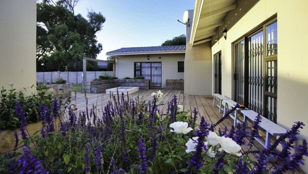 A modern house with a wooden deck, white benches, and purple flowers. - Sandy Feet Langebaan 8-sleeper (Langebaan)