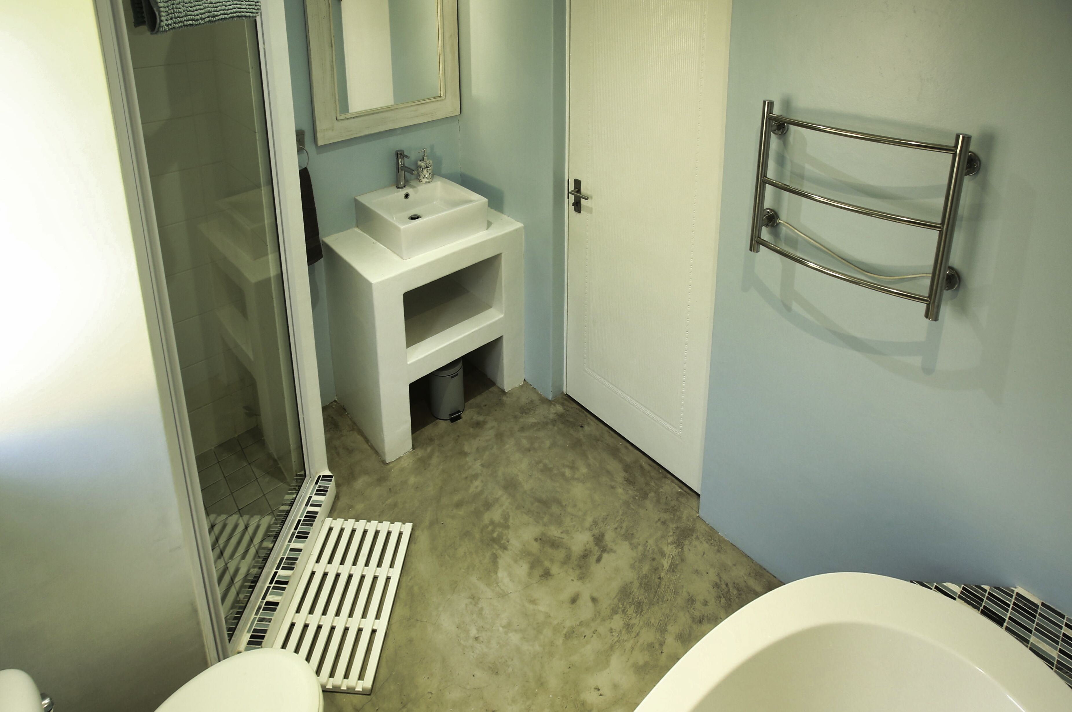 Une salle de bain avec un lavabo blanc, un miroir, un porte-serviettes, une douche et des toilettes.