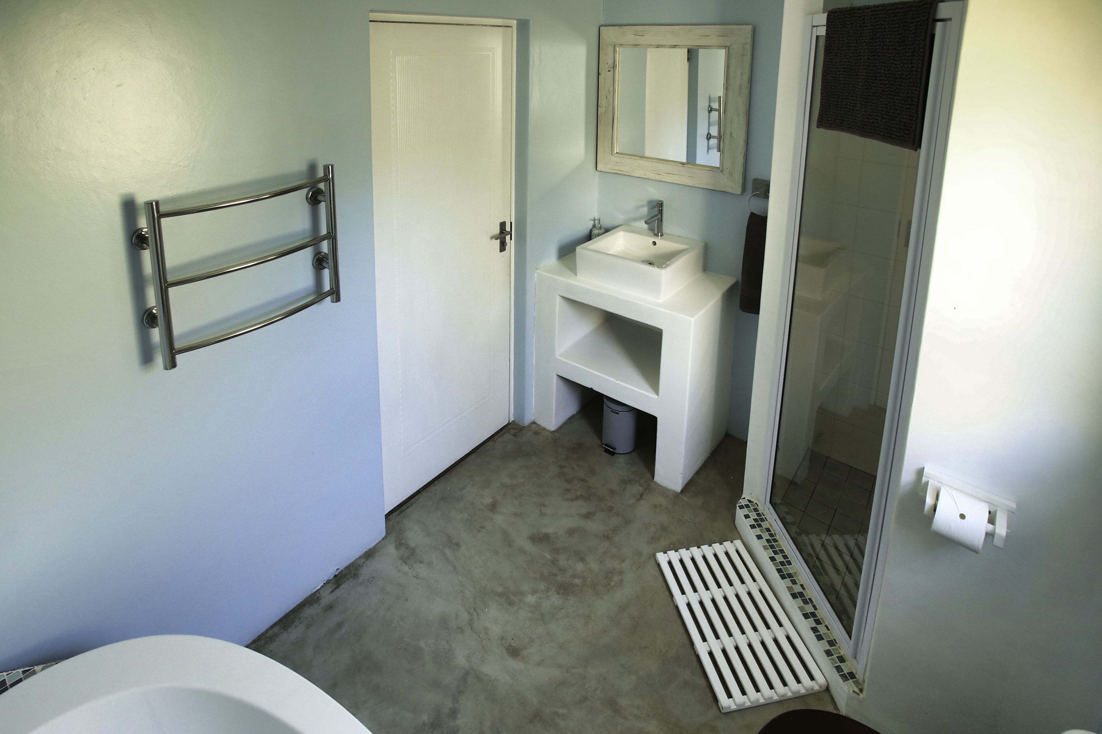 A bathroom with a white bathtub, a sink, a mirror, and a shower door.