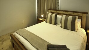 A neatly made bed with striped pillows, a patterned throw, and a dark towel. - Sandy Feet Langebaan 8-sleeper (Langebaan)