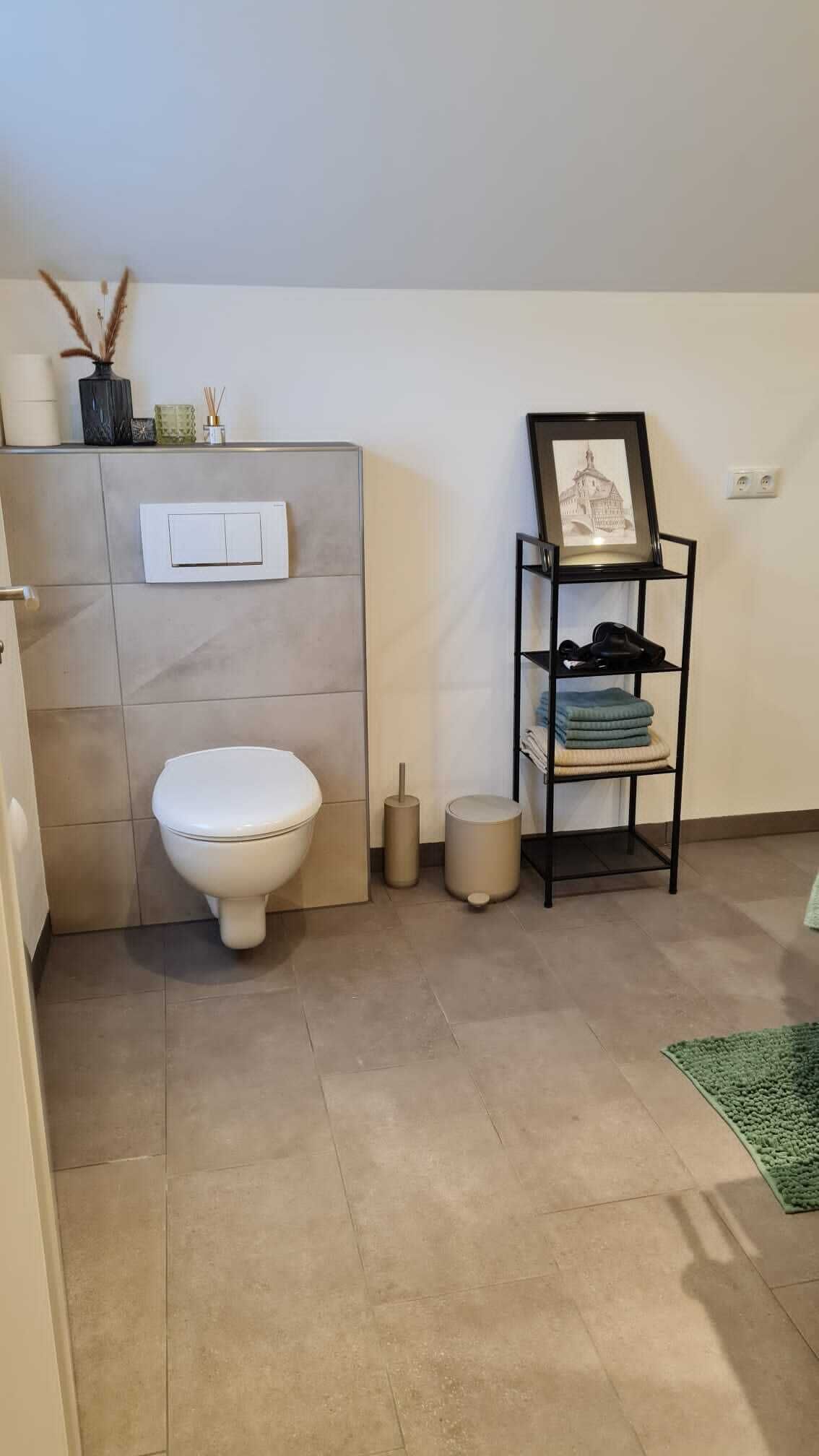 A bathroom with a toilet, a shelf with folded towels, and a framed picture on the wall.
