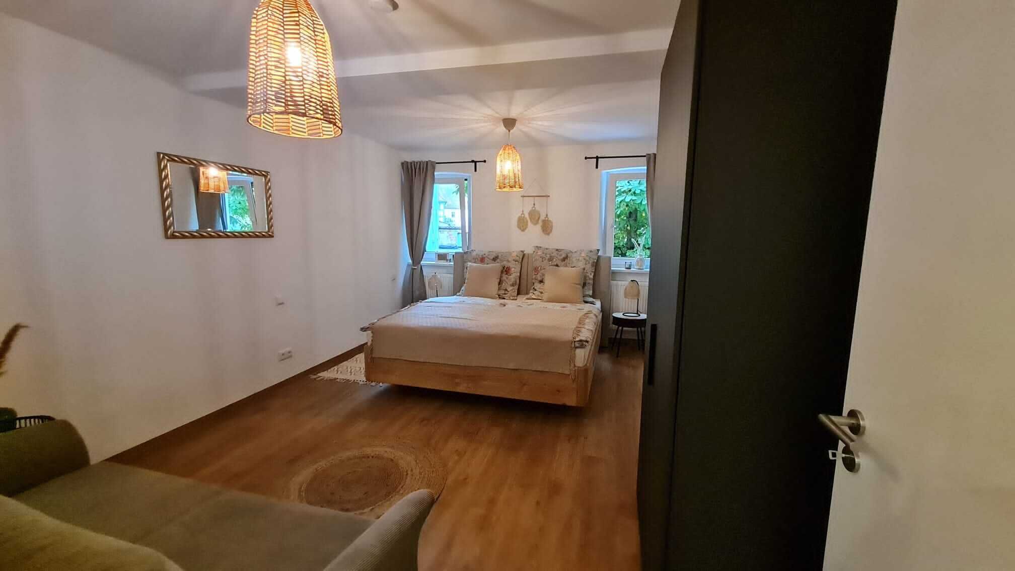 A bedroom with a bed, a chair, a small table, and a window.
