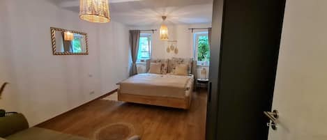 A bedroom with a bed, a chair, a small table, and a window.