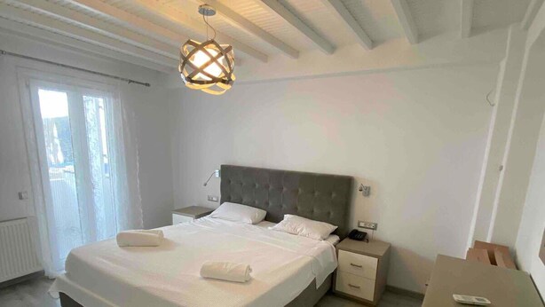 A bedroom with a large bed, a nightstand, a dresser, and a ceiling light fixture. - Mykonos Chora 2 Bd House Cycladic Escape (Mykonos)