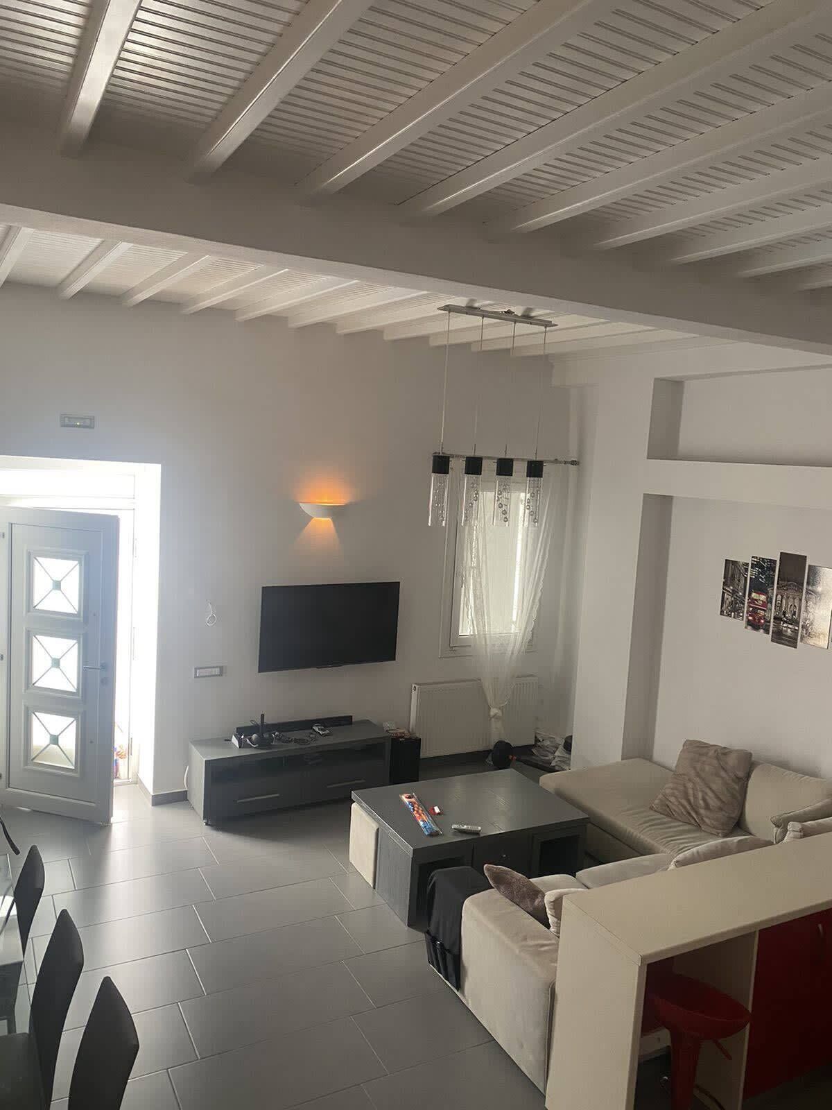 A modern living room with a sofa, coffee table, and TV. There is a door with glass panels and a window with curtains.