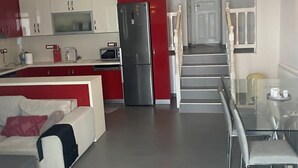 A modern kitchen with a red refrigerator, white cabinets, and a glass dining table. - Mykonos Chora 2 Bd House Cycladic Escape (Mykonos)