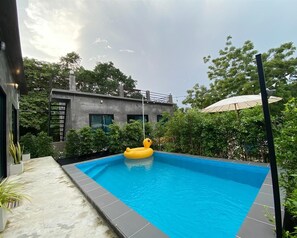 A rectangular swimming pool with a yellow inflatable duck, surrounded by greenery and a modern building in the background. - Rayong Pool Villa & Camping (Rayong)