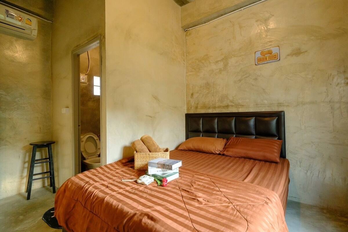 A bedroom with a bed, a small stool, a wicker basket, and a sign on the wall.