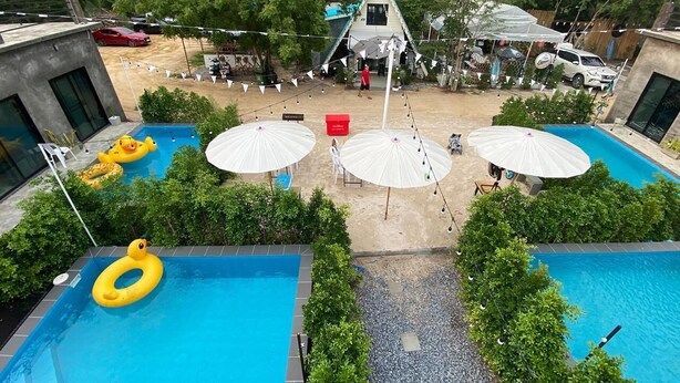 A pool area with two swimming pools, surrounded by greenery and umbrellas.