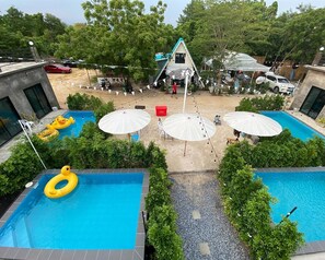 A pool area with two swimming pools, surrounded by greenery and umbrellas. - Rayong Pool Villa & Camping (Rayong)