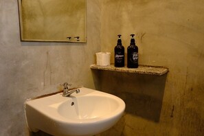 A bathroom with a white sink, a mirror, and two bottles of shampoo and body wash on a shelf. - Rayong Pool Villa & Camping (Rayong)