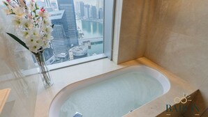 A bathroom with a bathtub, a vase of flowers, and a view of a cityscape through a window. - Elegant Studio Address Marina (Dubai)
