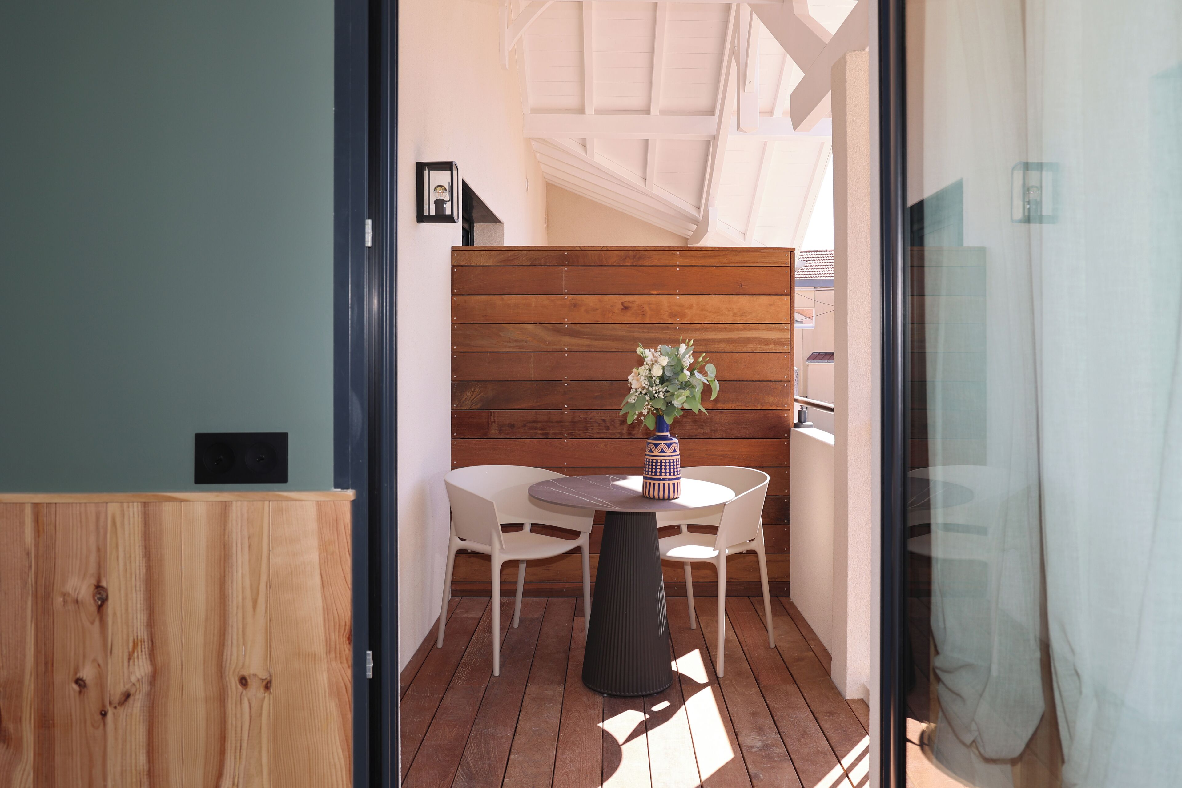 A small, enclosed patio area with a round table and two chairs, a wooden bench, and a potted plant.