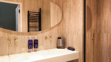 Une salle de bain moderne avec un grand miroir ovale, un lavabo blanc et une pomme de douche dorée.