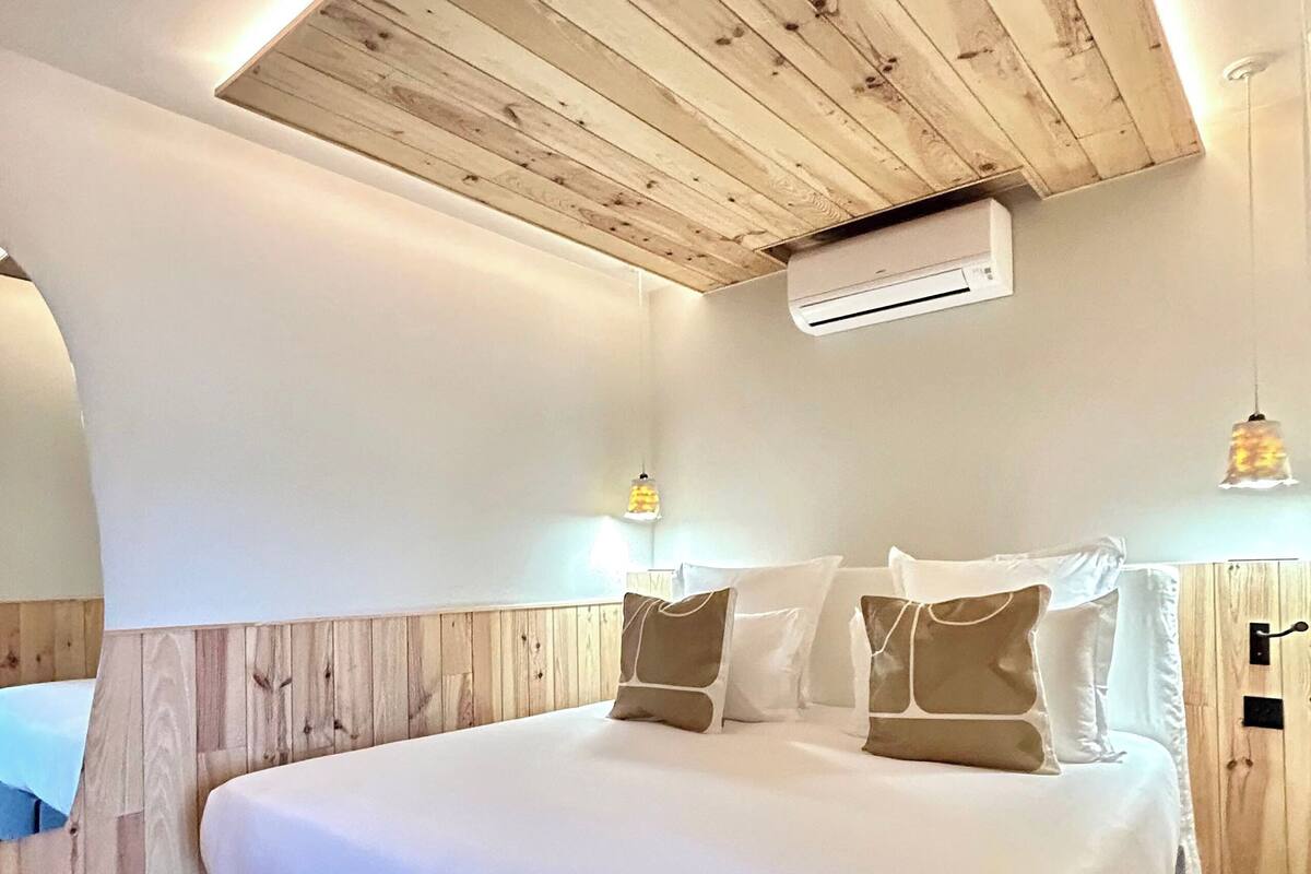 A bedroom with a wooden ceiling, a bed with white bedding, and an air conditioning unit.