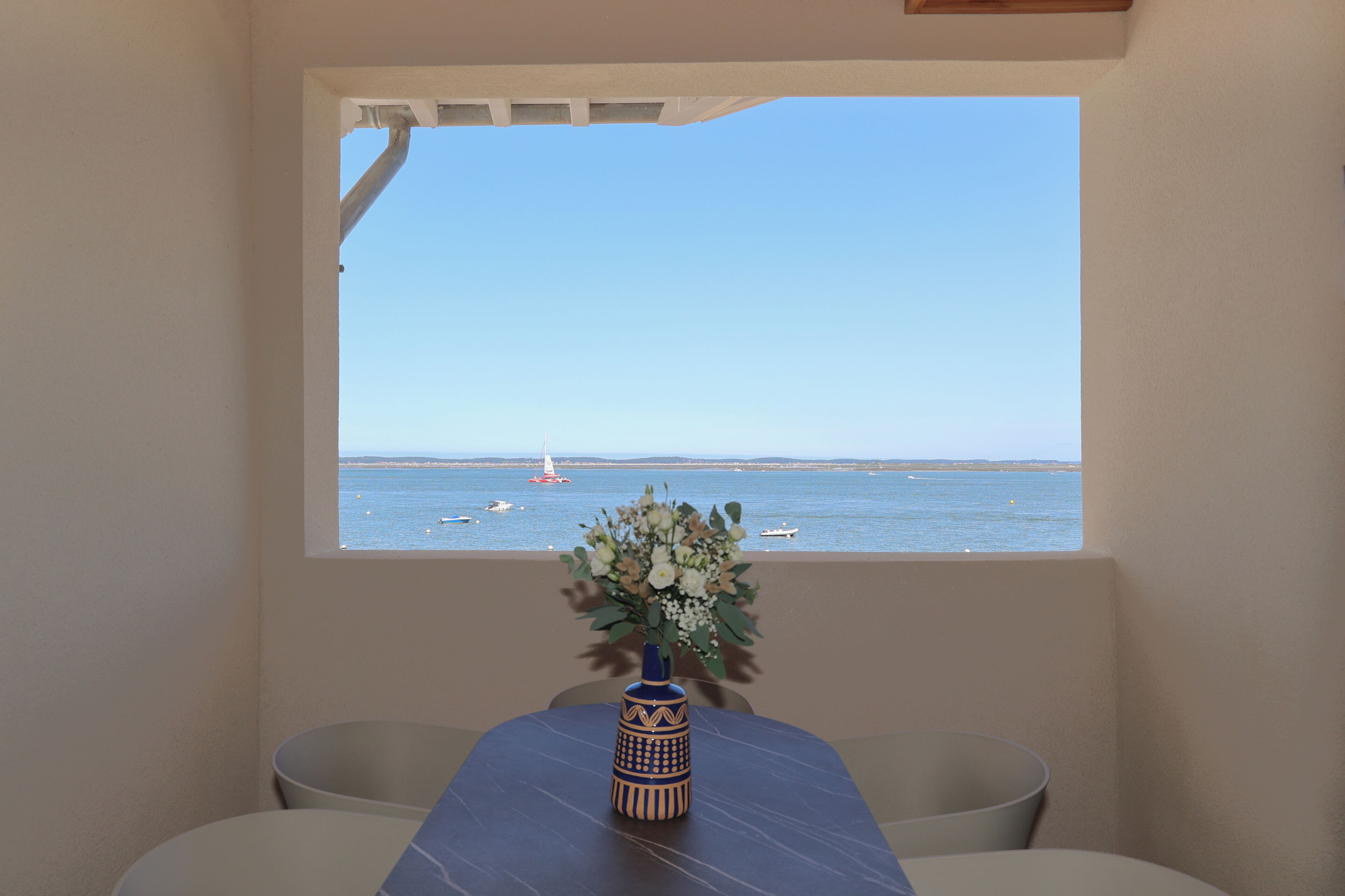 Une pièce avec vue sur la mer, une table ornée d’un vase de fleurs et une chaise.