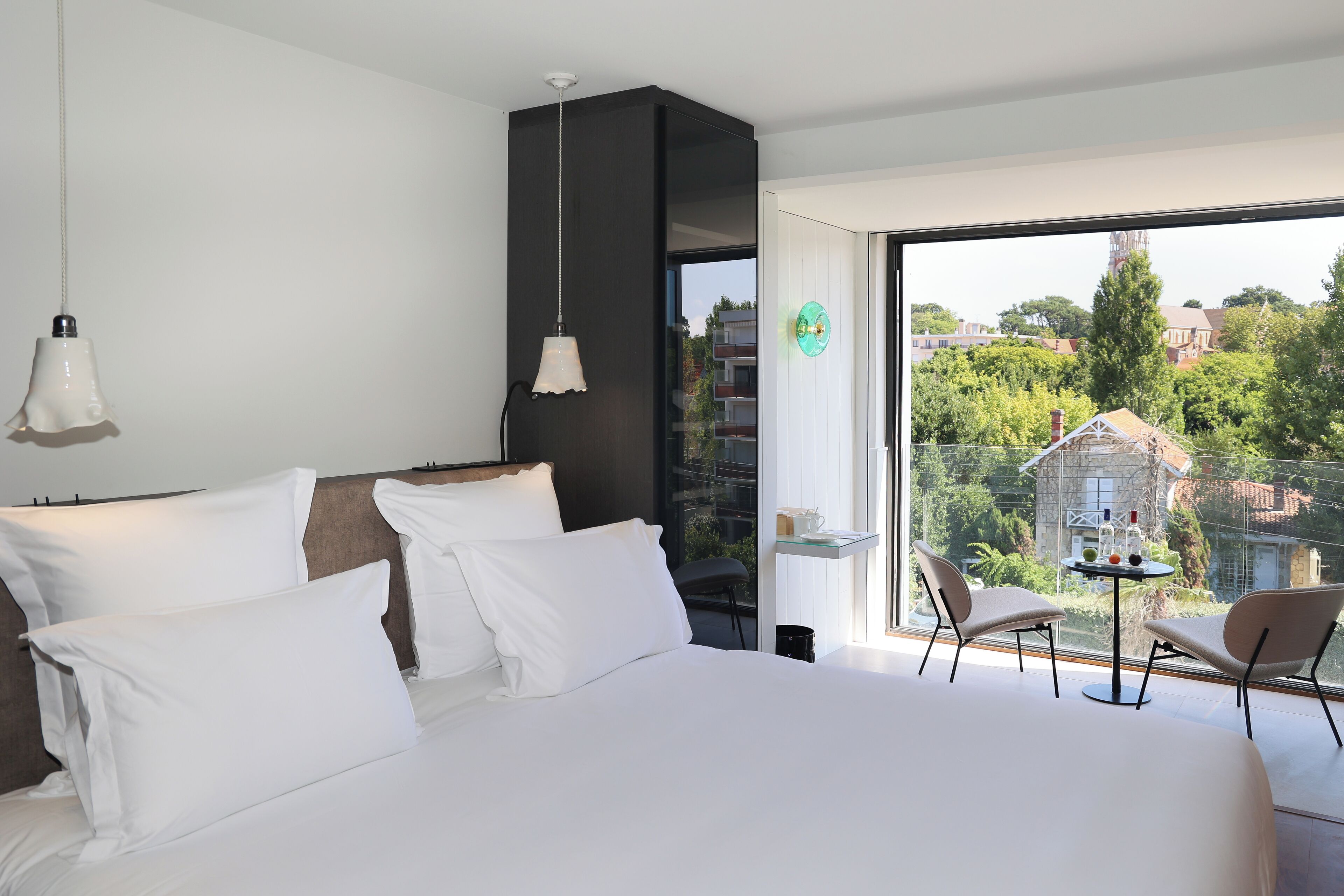 A modern bedroom with a large bed, two bedside tables, and a view of a balcony with a table and chairs.