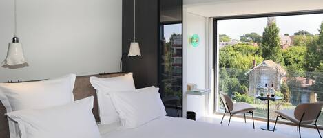 A modern bedroom with a large bed, two bedside tables, and a view of a balcony with a table and chairs.