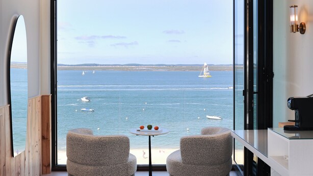 Una habitación moderna con un amplio ventanal con vistas al mar, que incluye dos sillas y una mesita.