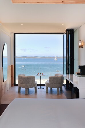 Una habitación moderna con un amplio ventanal con vistas al mar, que incluye dos sillas y una mesita.