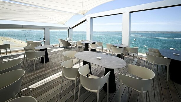 A deck with tables and chairs overlooking the ocean. - Les Vagues Hôtel & Spa (Arcachon)