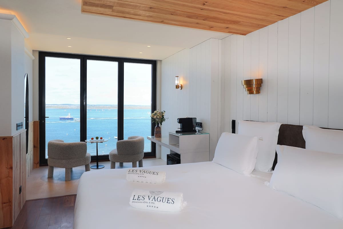 A hotel room with a large bed, a desk, a chair, and a view of the sea.