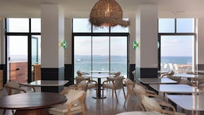 Un restaurante con vista al mar, con mesas redondas y sillas de mimbre.