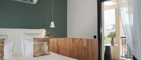 A bedroom with a wooden headboard, a bed with white bedding, a hanging pendant light, and a view of a balcony with a table and potted plant.