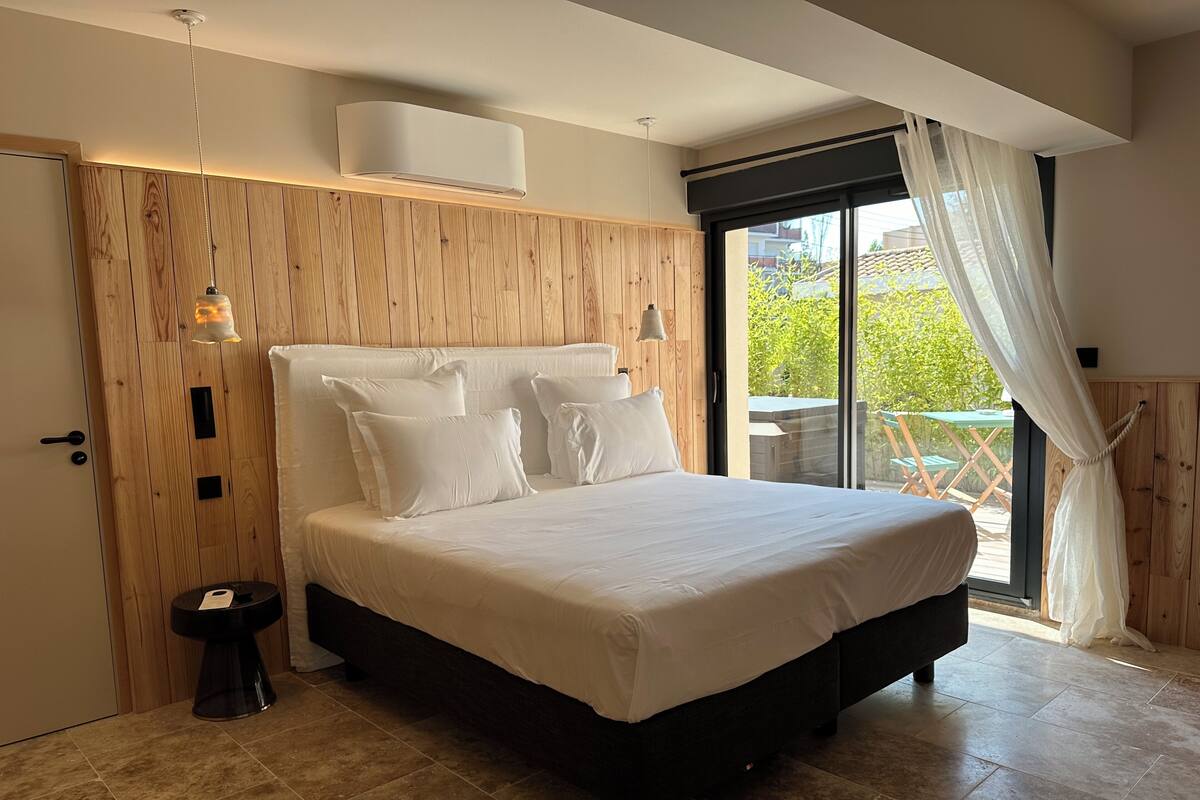 A modern bedroom with a large bed, wooden panel walls, and a sliding glass door to a balcony.