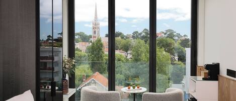 A modern room with large windows, two chairs, a small table, and a view of a church tower.
