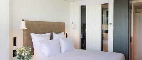 Habitación de hotel con una cama grande, ropa de cama blanca, un florero con flores y un espejo en la pared.