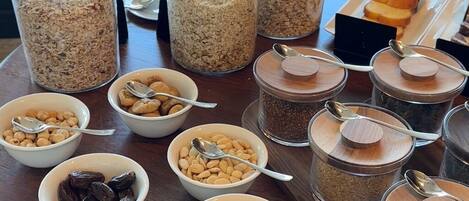 Una mesa de buffet con diversos alimentos y recipientes, incluyendo cuencos con frutos secos, frutas deshidratadas y cereales.