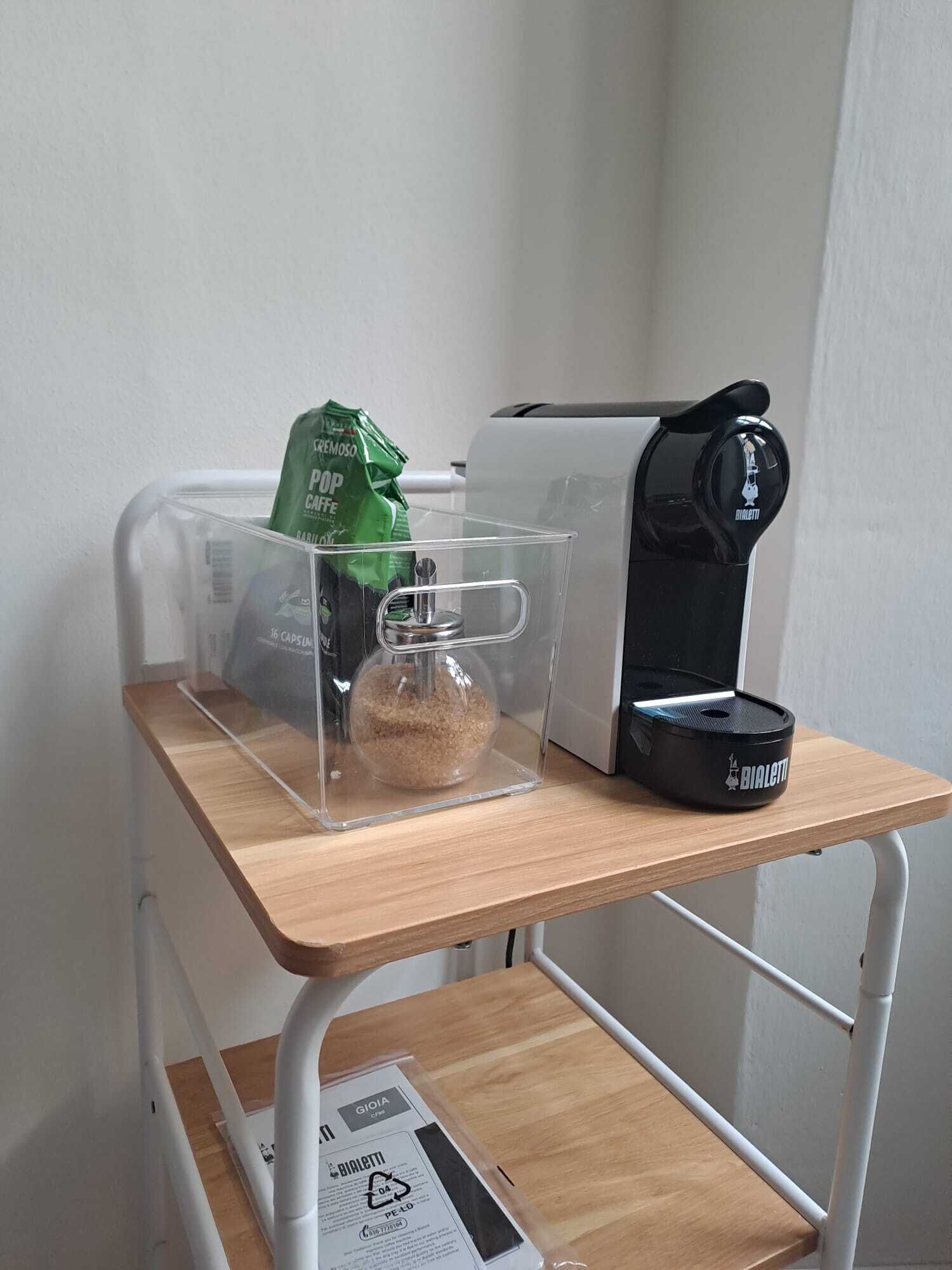 A small kitchenette with a coffee maker, a clear container with a glass lid, and a bag of coffee.