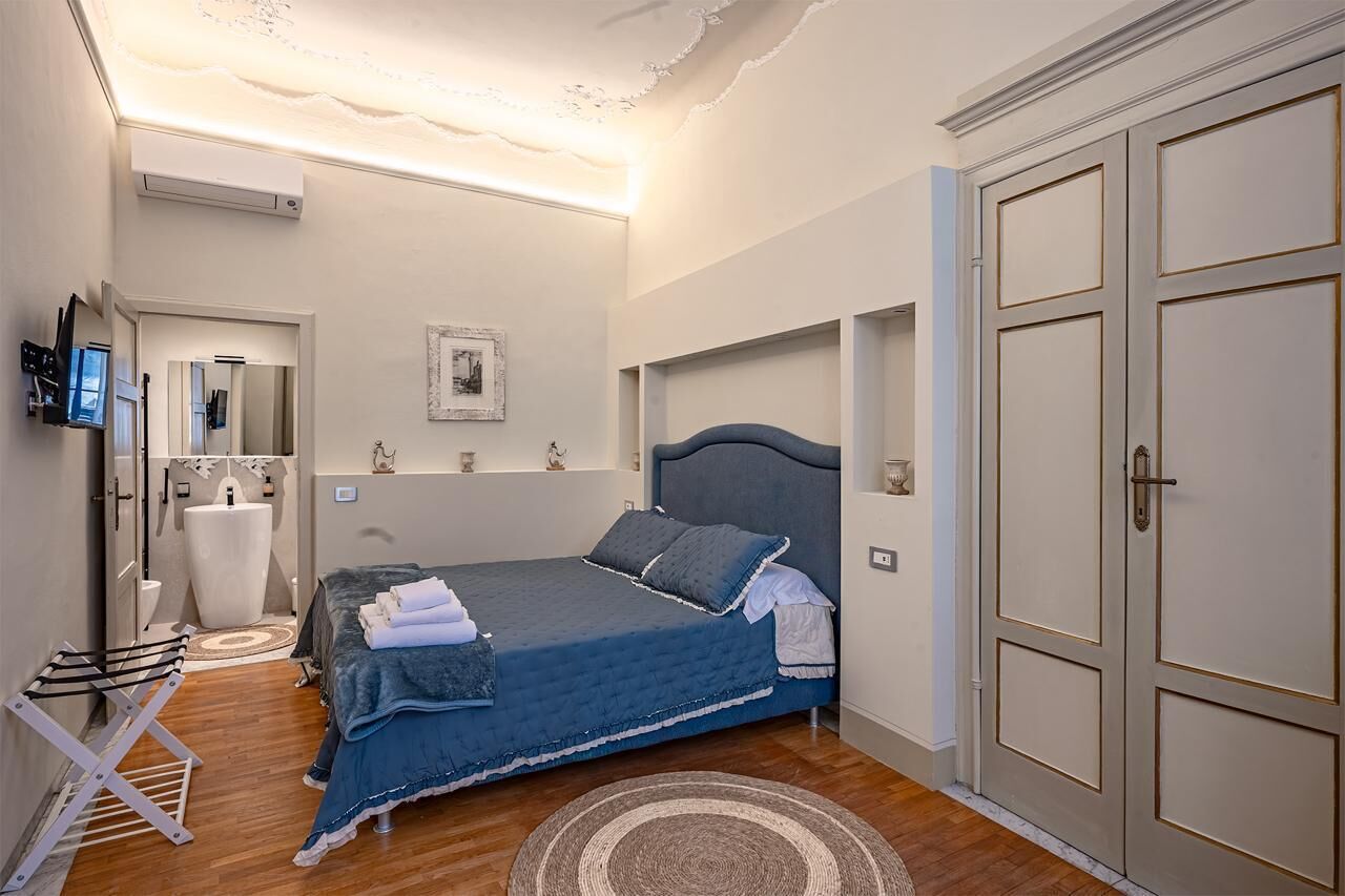 A bedroom with a bed, a wardrobe, a mirror, a television, and a bathroom with a sink and toilet.