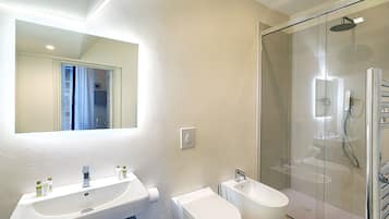 A modern bathroom with a large mirror, two sinks, a toilet, a bidet, and a glass-enclosed shower.
