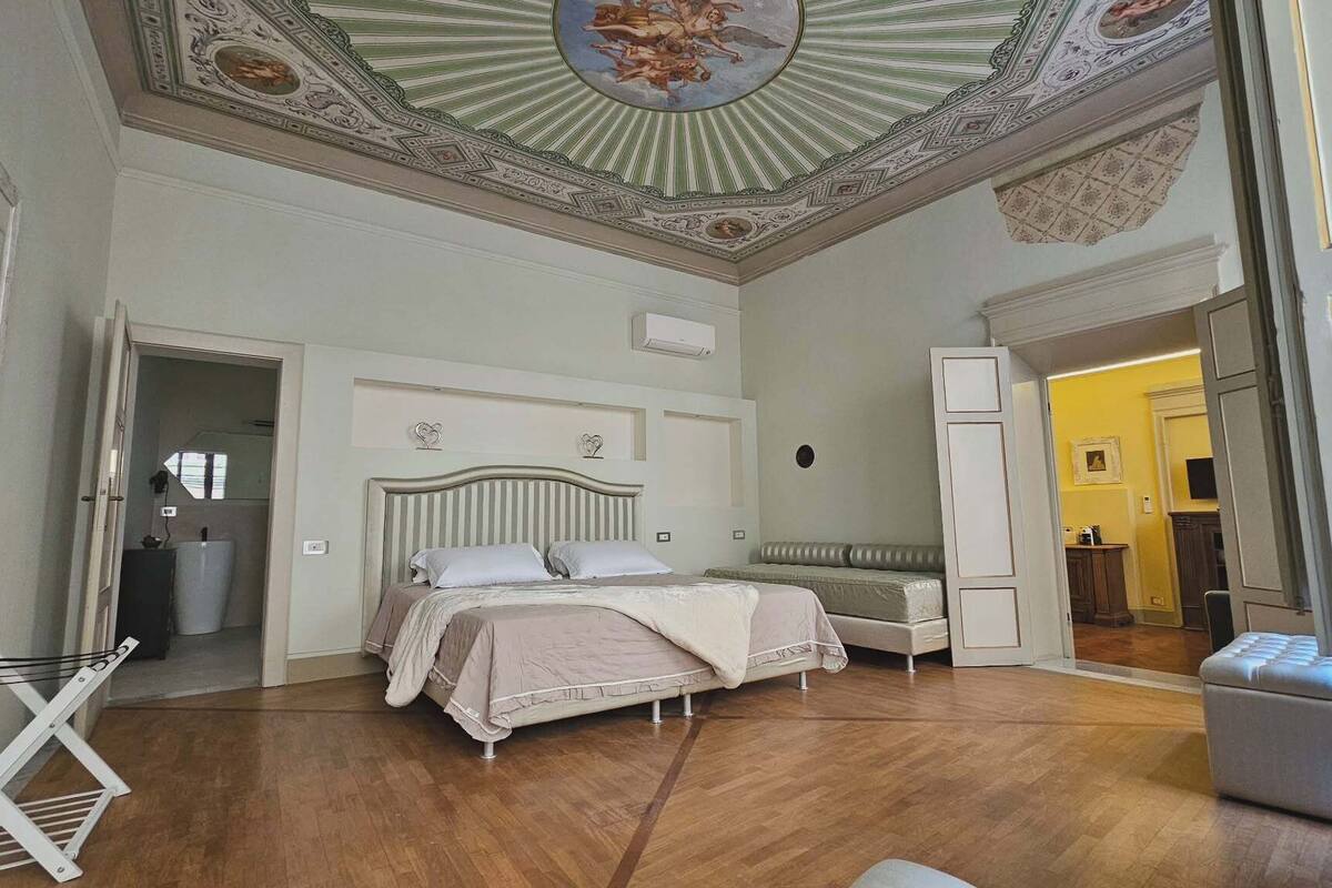 Ein Schlafzimmer mit einem großen Bett, einem Kleiderschrank, einem Heizkörper und einer kunstvoll gestalteten Decke.