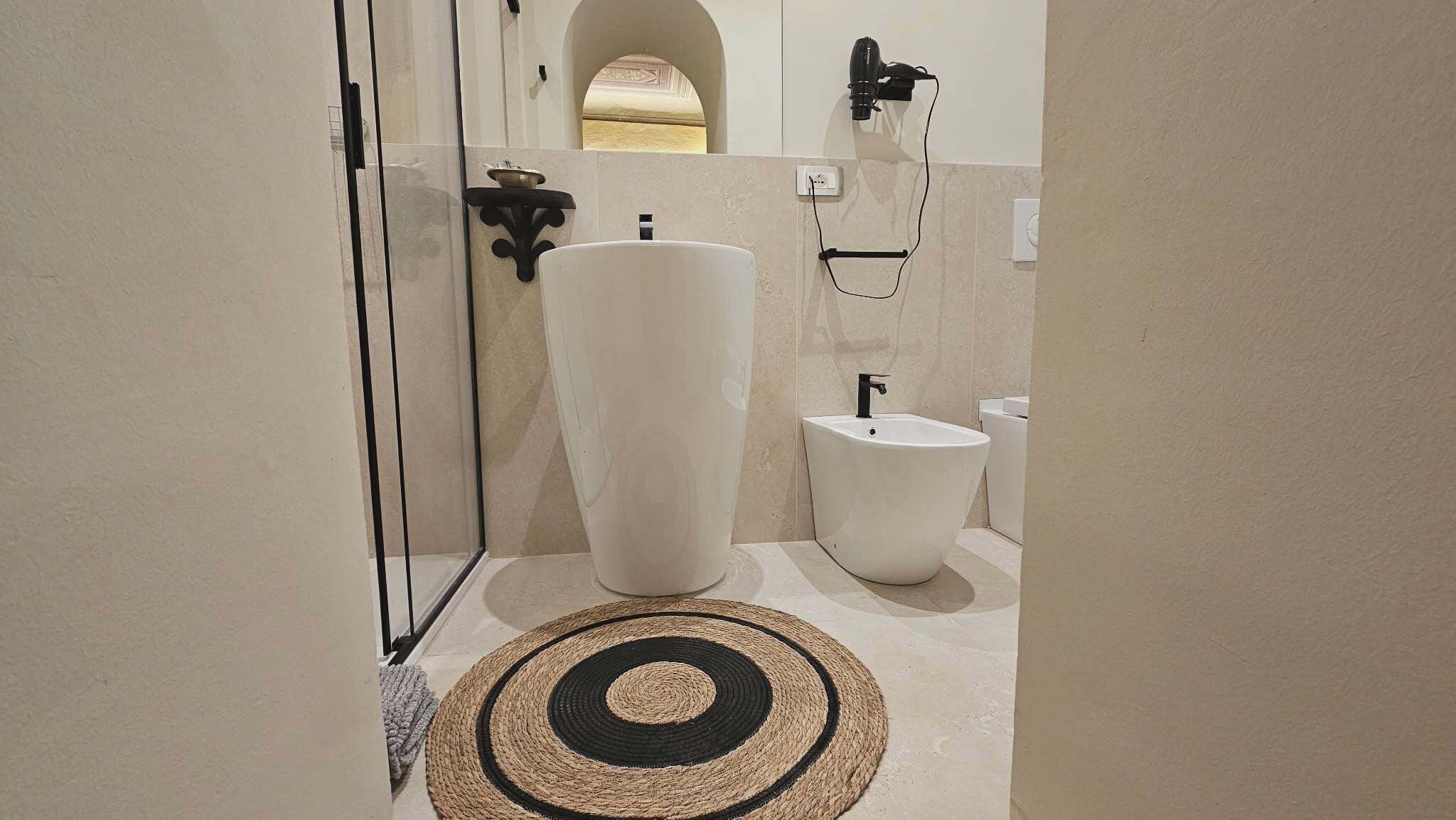Un baño con un lavamanos grande de color blanco, un bidé y un perchero para toallas.