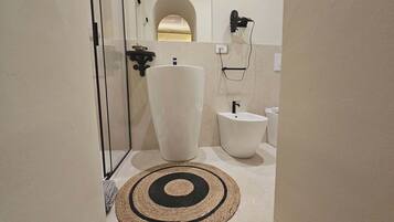 Un baño con un lavamanos grande de color blanco, un bidé y un perchero para toallas.
